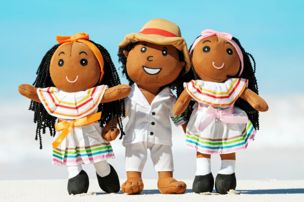Fabric dolls wearing a white cotton ensemble with bands of color at the beach.