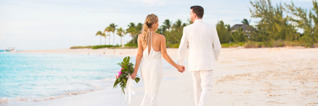 Newlywed couple walking along the beach in Turks and Caicos at sunset. 