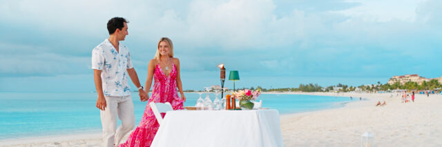 Couple at a candlelit table on Grace Bay Beach, sunset.