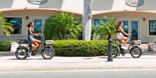 Women riding electric bicycles in Turks and Caicos past shops. 