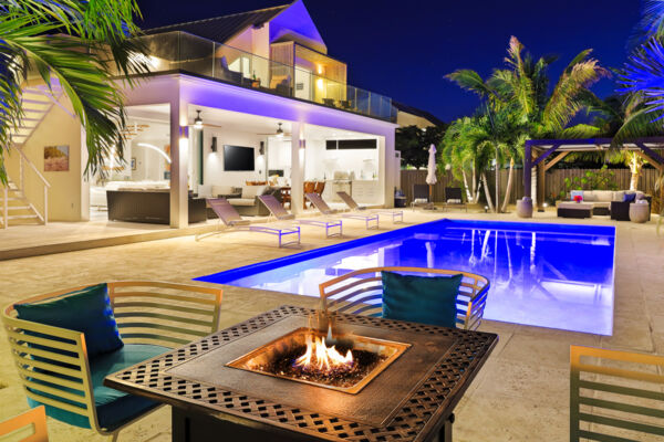 Fire table and chairs adjacent to a pool at a luxury villa at night.