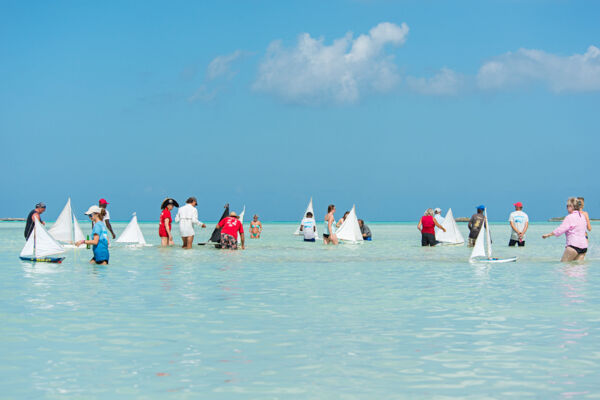 People racing model sailboats on Bambarra Beach, Middle Caicos. 