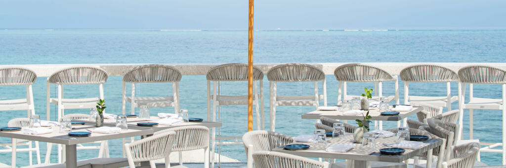 A row of chairs lined up beneath a terrazzo bar that overlooks a turquoise ocean. 