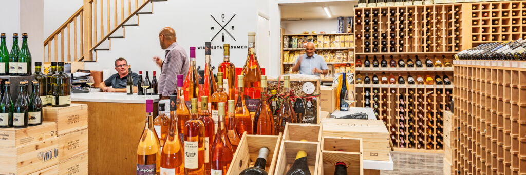 A customer samples a glass of white wine in a bright and cozy wine store.