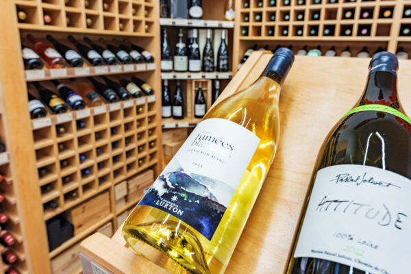 A bottle of white wine on a wooden shelf at a bright and cozy wine shop.