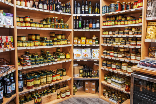 Shelves filled with olives, cooking oils, mustards, and preserves in a wine store.